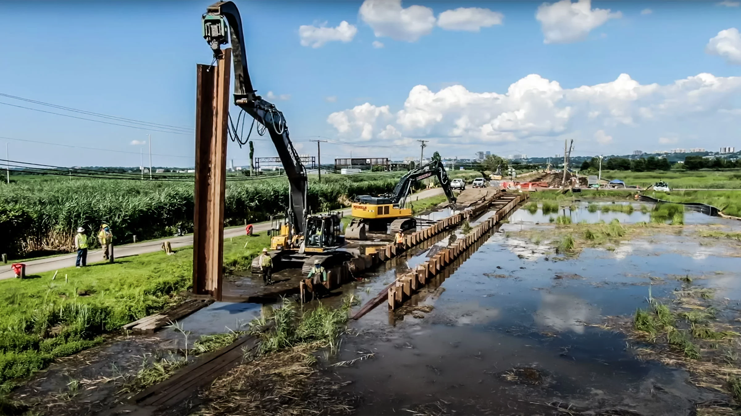 Excavators working alongside a road near a marsh.