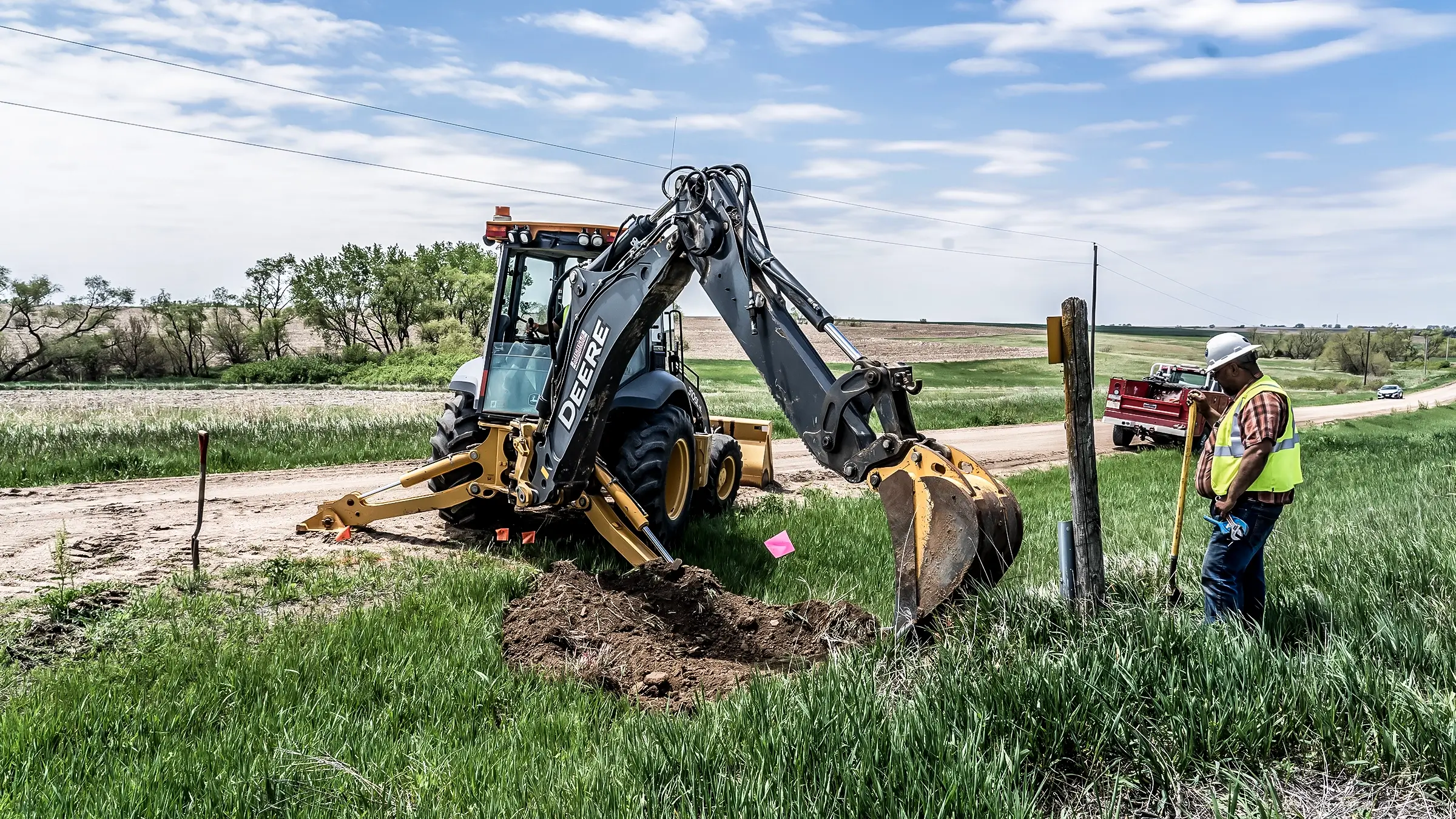 A crew member and small excavator assist in byurying a cable line.
