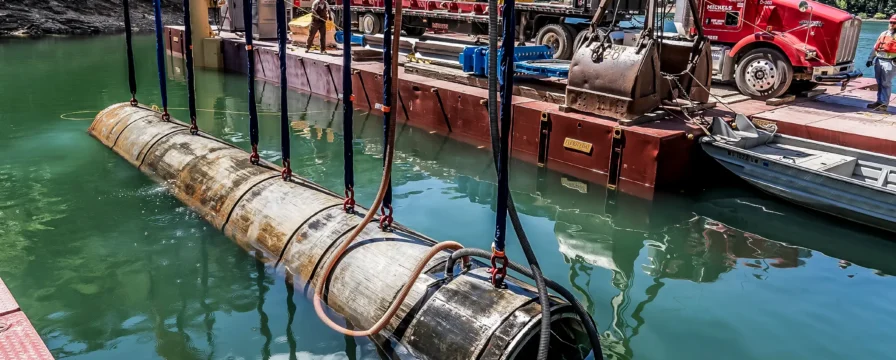 A piece of directional drilling equipment being lifted out of a body of water by cranes on a barge.